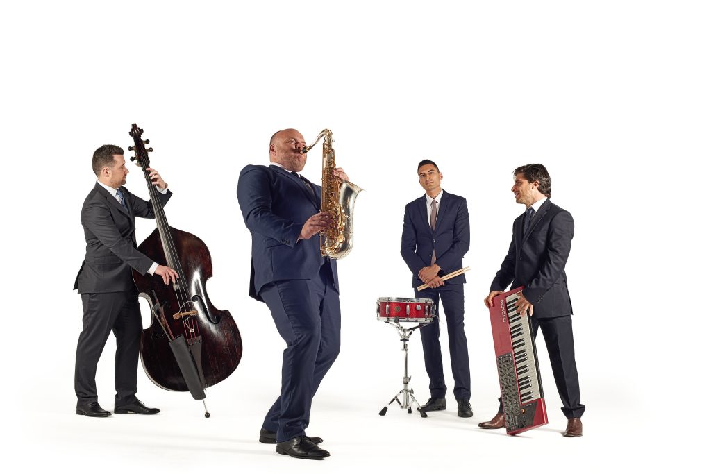 The Graduates jazz quartet performing, featuring saxophone, keyboard, bass and drums.